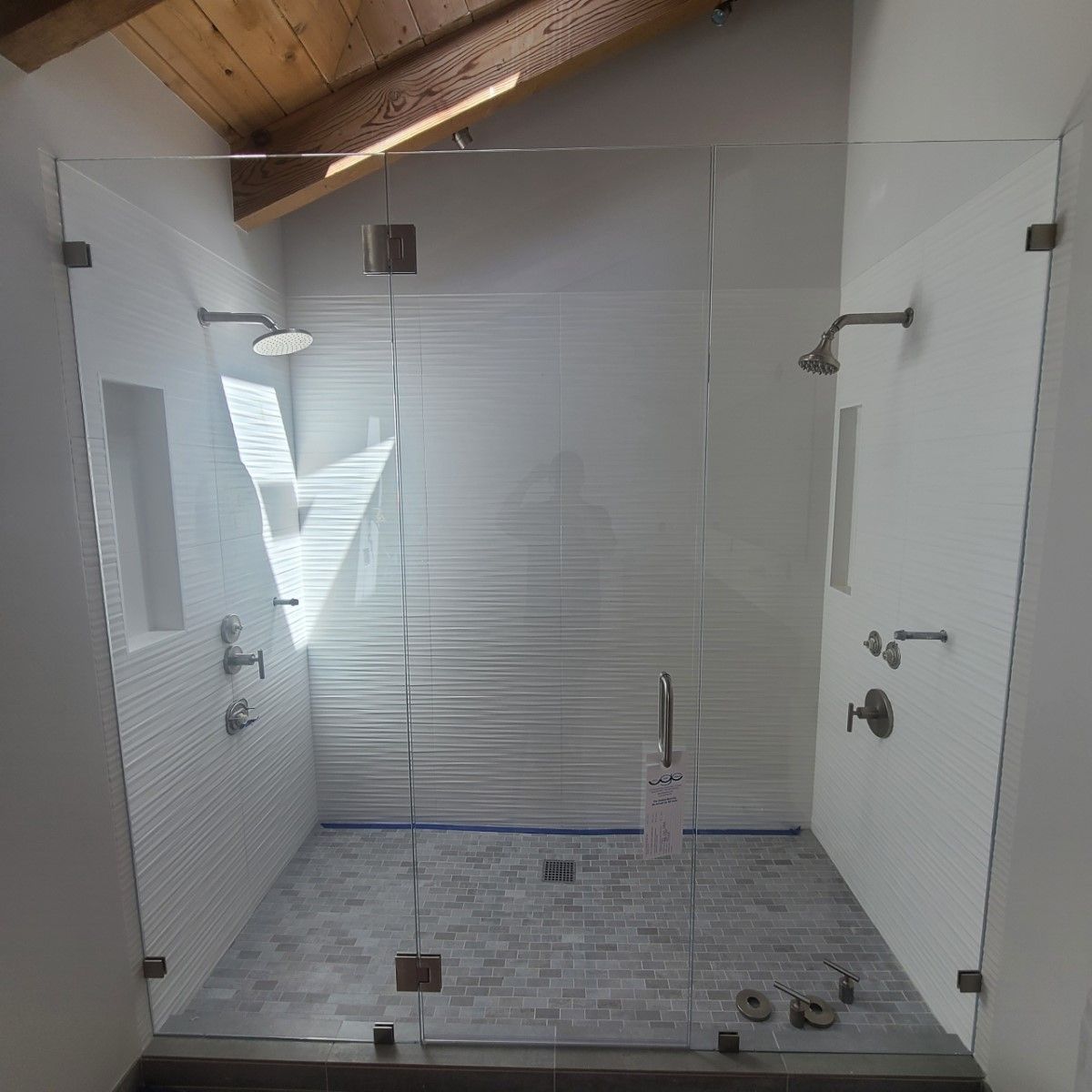 Empty tiled shower stall with glass door, chrome fixtures, and white walls beneath a wood-beamed ceiling