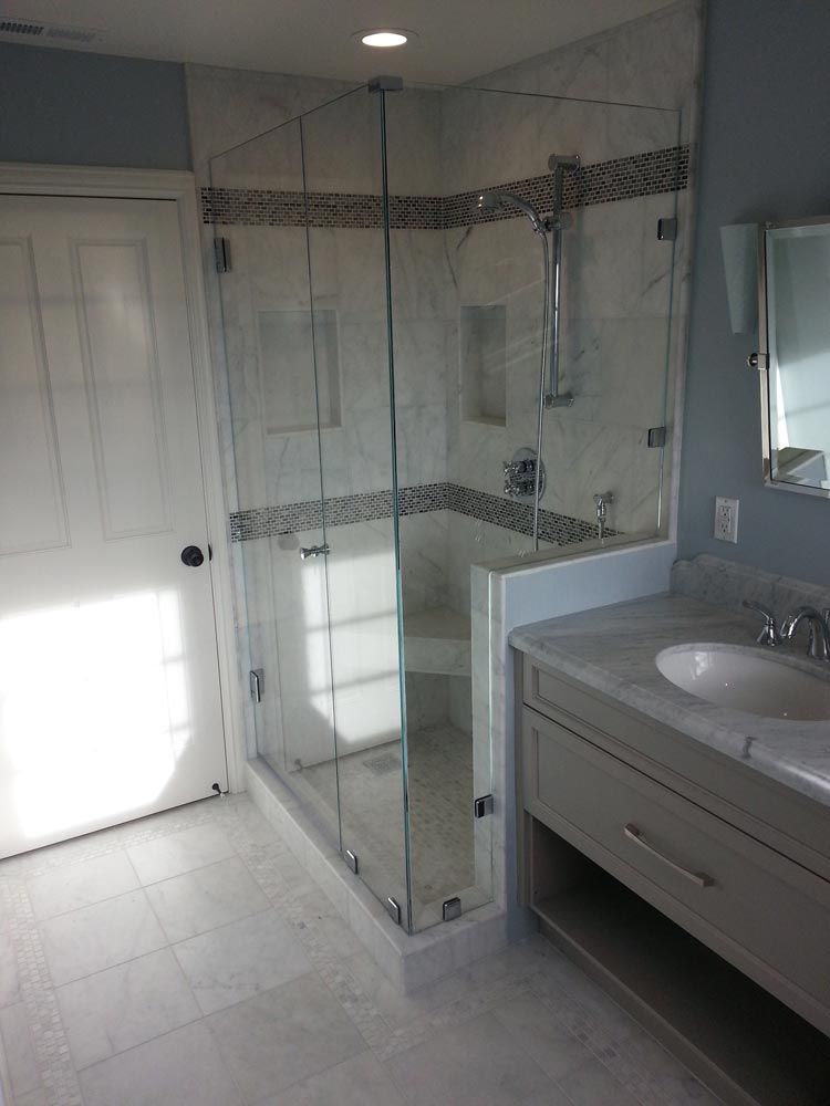 Bright bathroom with glass-enclosed shower, vanity sink, mirror, and white tile floor.