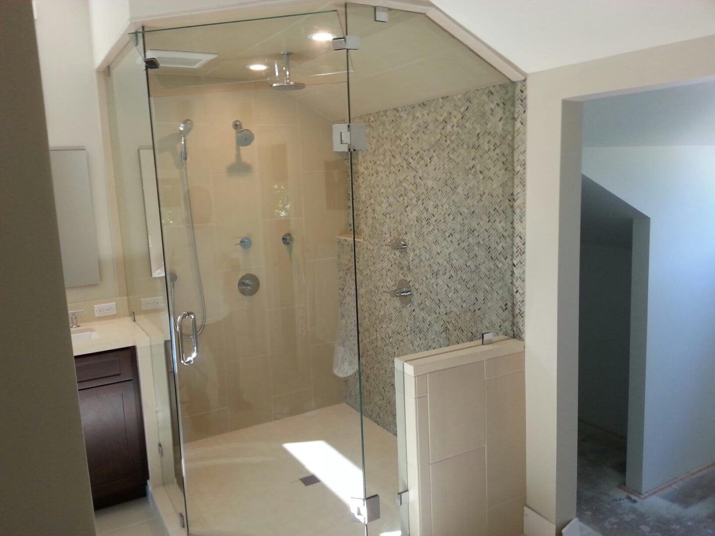 Modern bathroom with glass-enclosed shower, beige tile, and mosaic accent wall