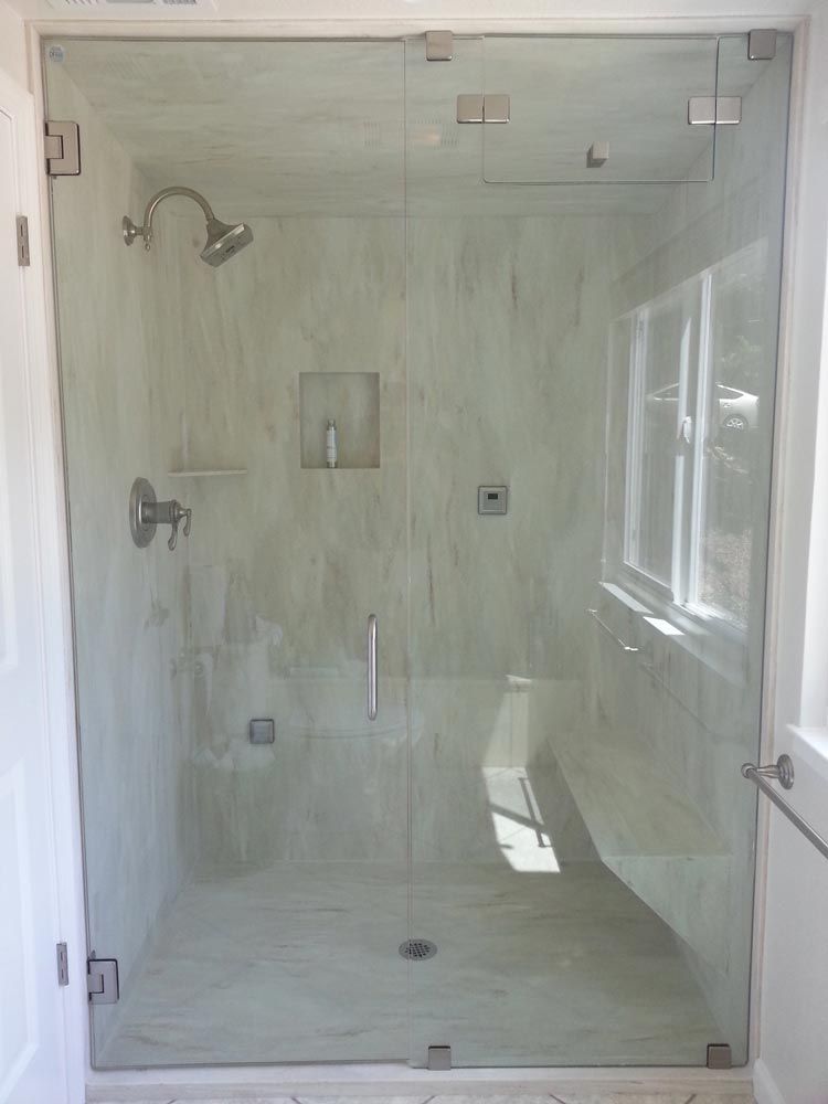 Walk-in glass shower with marble-look tile, grab bars, and built-in niche in a bright bathroom