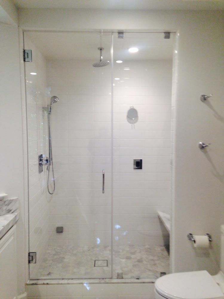 Glass walk-in shower with white tile, chrome fixtures, and partial toilet visible in a bathroom