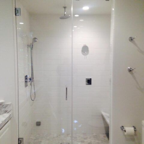 Modern walk-in shower with clear glass doors, white tile walls, and handheld showerhead.