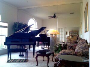 Grand piano in a bright living room with floral sofa, round table, and ceiling fan