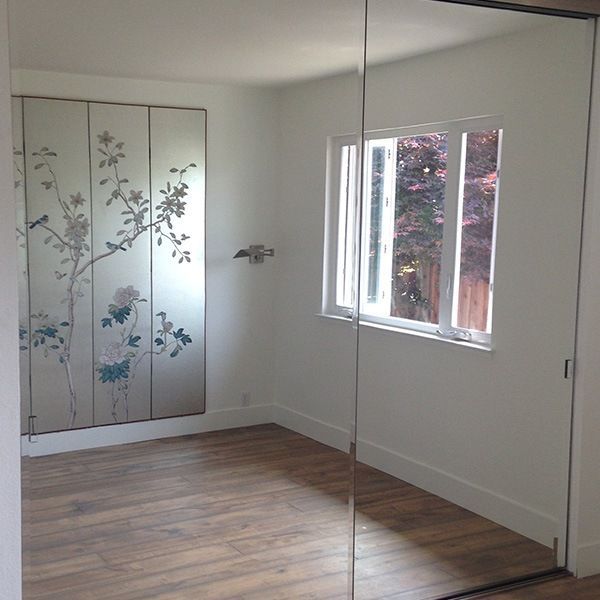 Empty bedroom with wood floors, mirrored closet doors, floral wardrobe, and a window letting in daylight.
