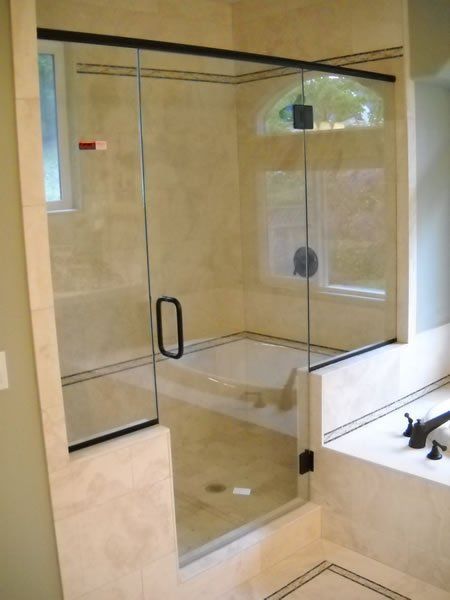 Glass-enclosed beige shower with a black handle and built-in bench, viewed in a bathroom.