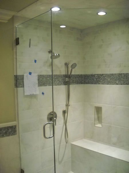 Glass walk-in shower with beige tile, chrome fixtures, grab bar, and built-in bench.
