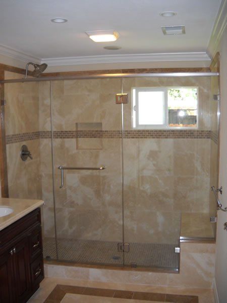 Tiled walk-in shower with glass door, bench, and small window in a beige bathroom