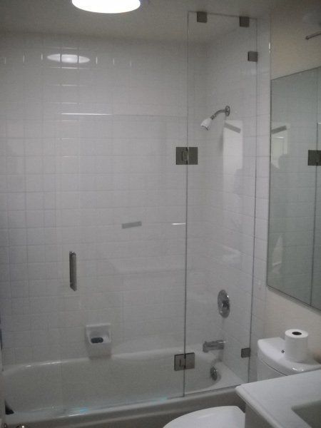 White tiled bathroom with a glass shower enclosure, wall-mounted showerhead, and toilet paper holder.
