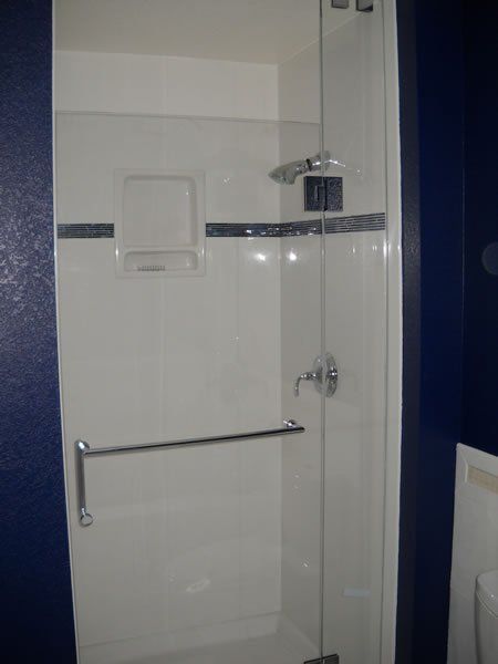 White tiled shower stall with grab bar, handheld showerhead, and built-in shelf