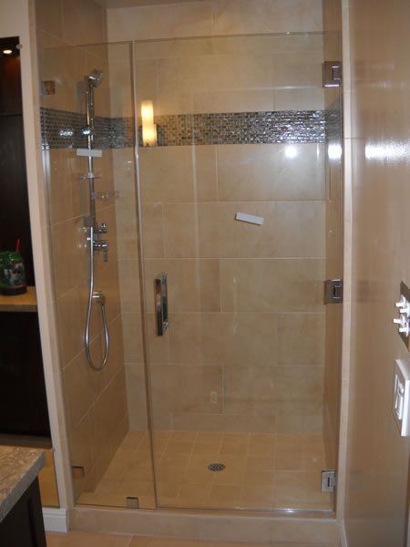 Glass shower stall in beige-tiled bathroom with chrome fixtures and a patterned accent strip.