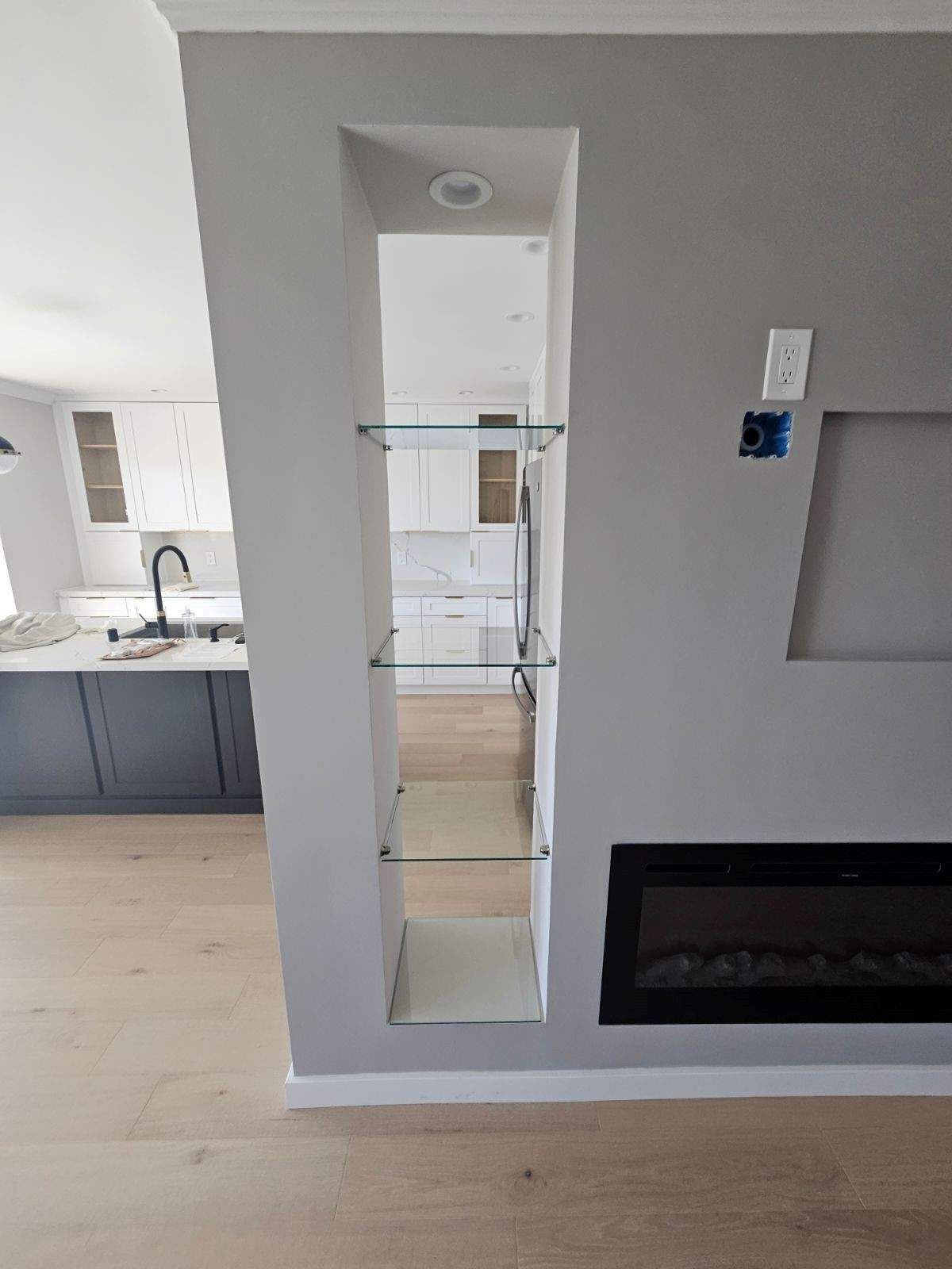 Modern living room with a narrow wall mirror, fireplace, and view into a bright kitchen.