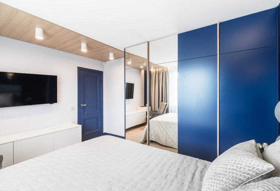 Modern bedroom with blue wardrobes, a wall-mounted TV, and white bedding