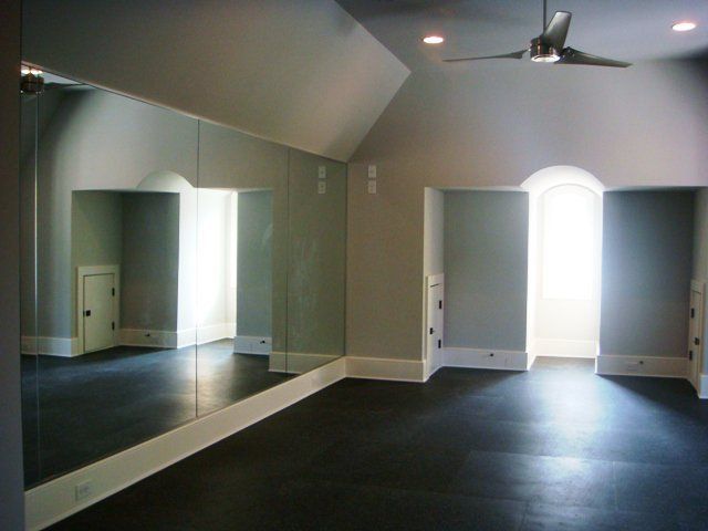 Empty room with dark carpet, mirrored wall, and bright arched window.