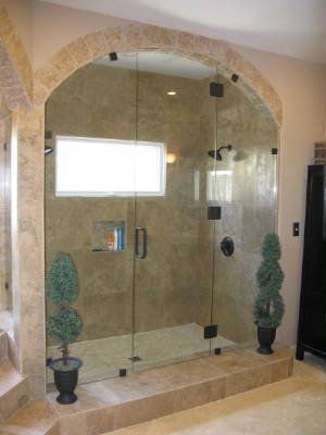 Glass shower enclosure with tiled walls and two potted topiary plants on a raised ledge