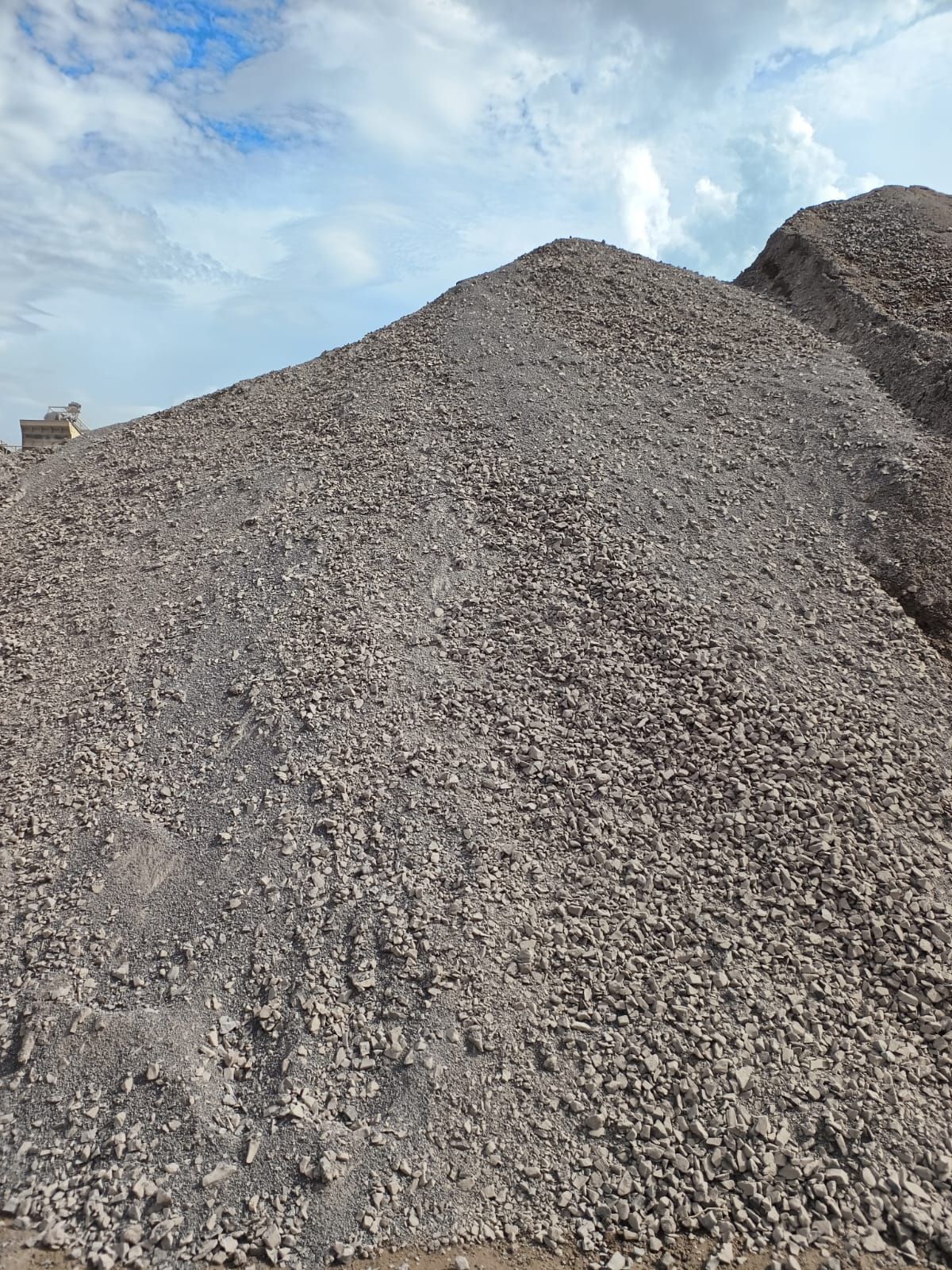 Montón de grava gris contra un cielo azul parcialmente nublado.