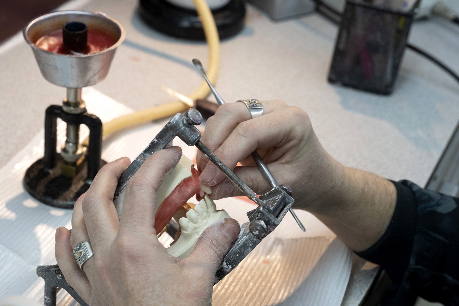 Des mains manipulent des outils sur un modèle dentaire ; la scène semble se dérouler dans un laboratoire dentaire.