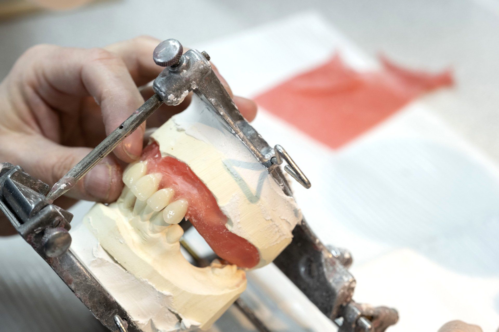 Un modèle dentaire avec des dents artificielles dans un dispositif articulé, tenu par une personne. De la cire rouge est visible.