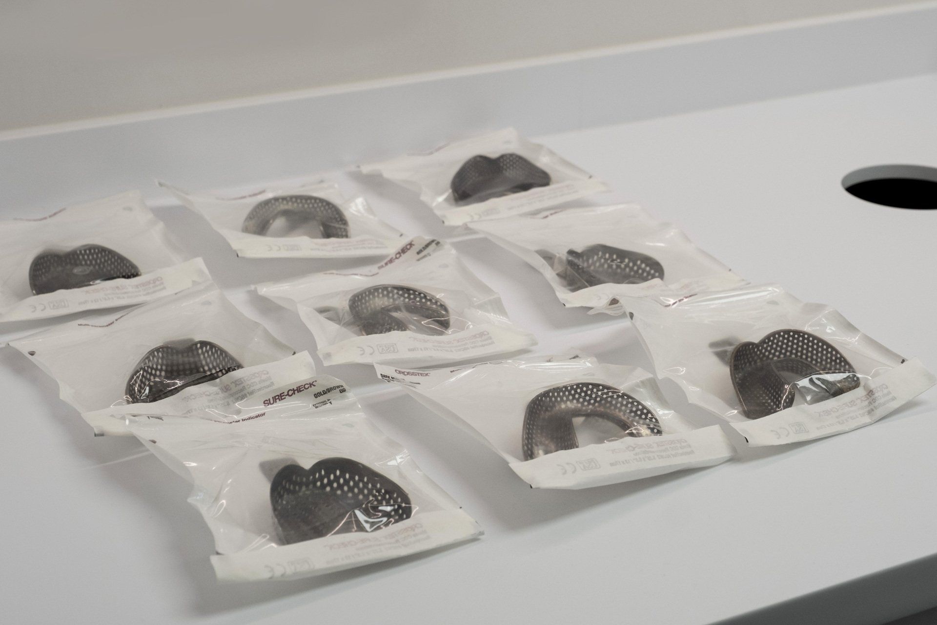 Neuf implants dentaires en métal dans des sachets en plastique scellés, posés sur une surface blanche.
