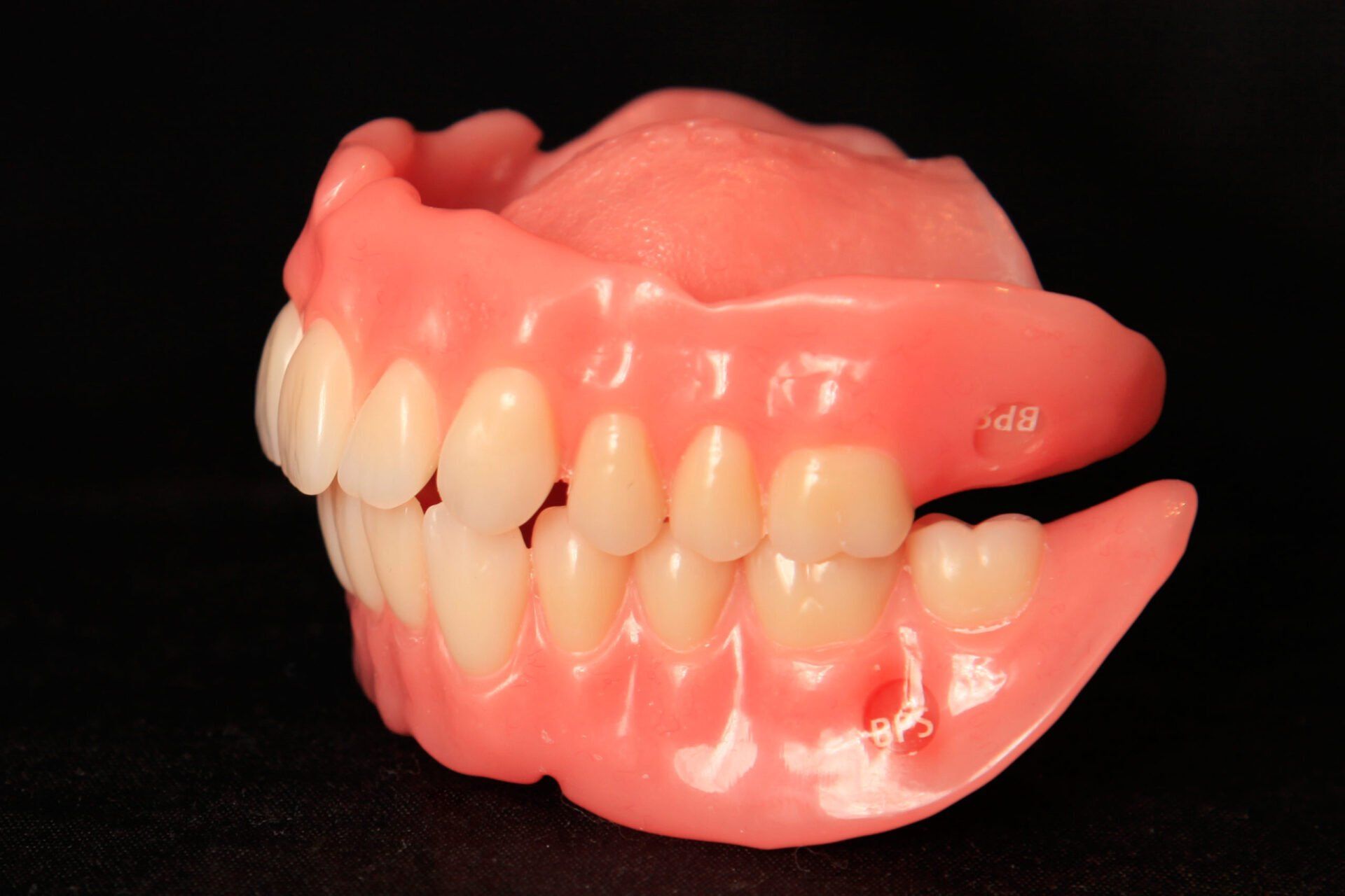 Prothèse dentaire complète, en plastique rose avec dents, sur fond noir.