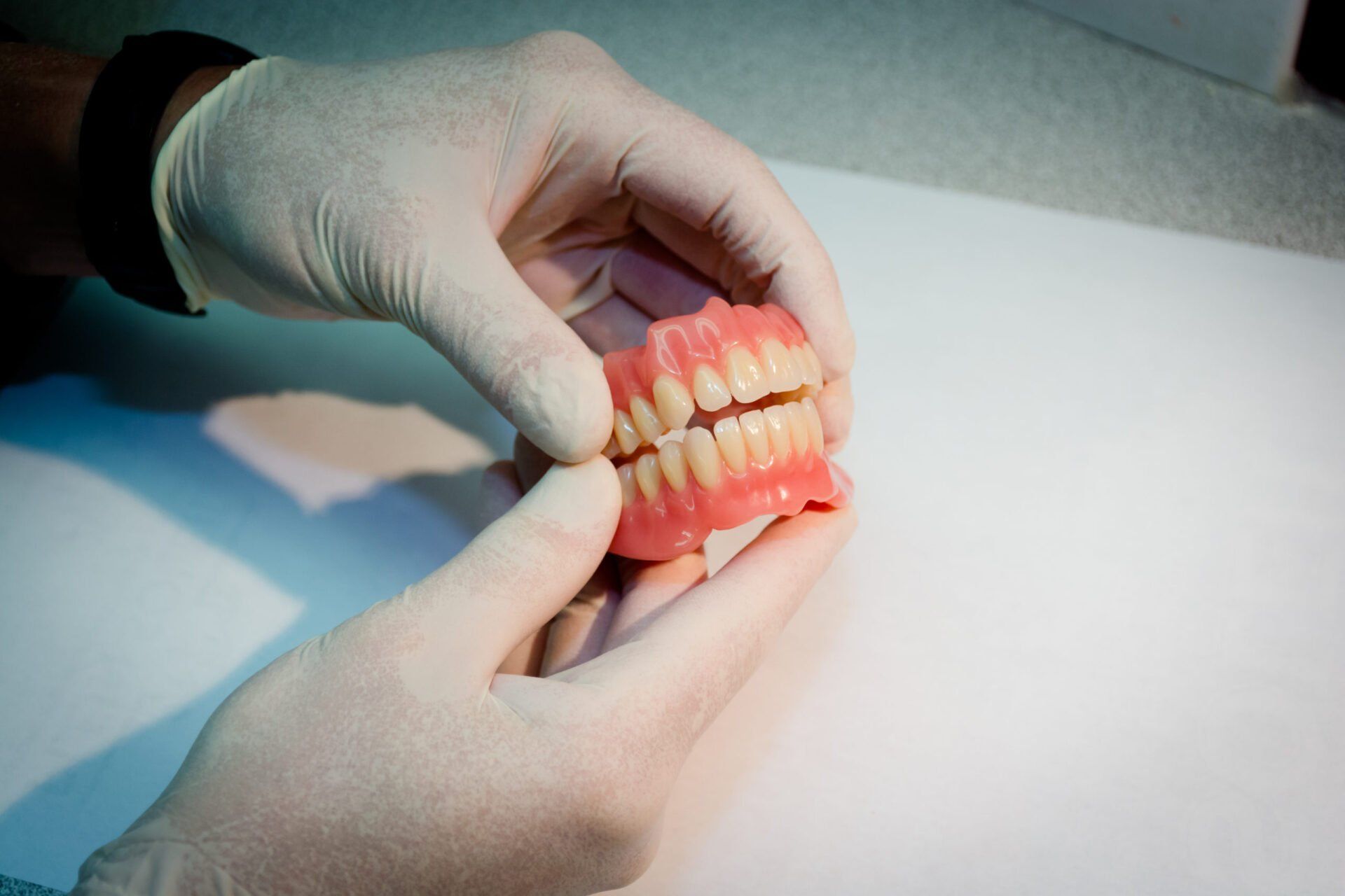 Des mains gantées de blanc tenant un dentier.