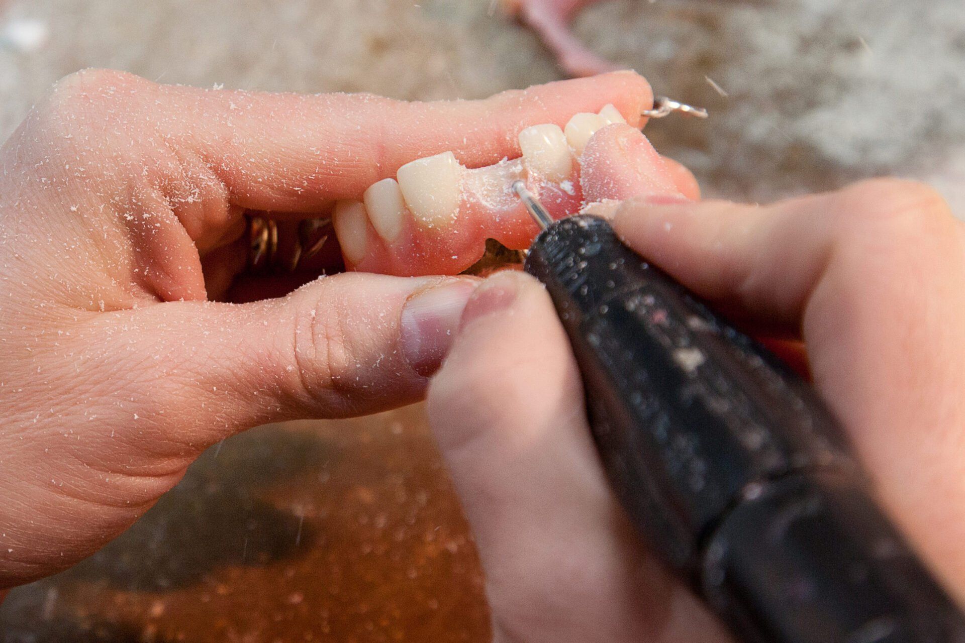 Des mains tenant des prothèses dentaires, utilisant une fraise dentaire pour façonner et affiner les dents.