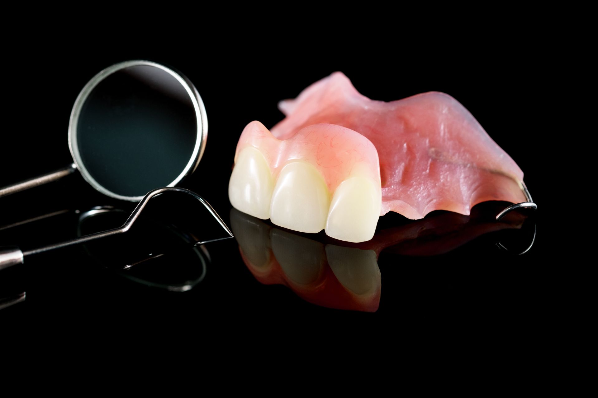 Instruments dentaires et prothèses partielles sur une surface noire réfléchissante.