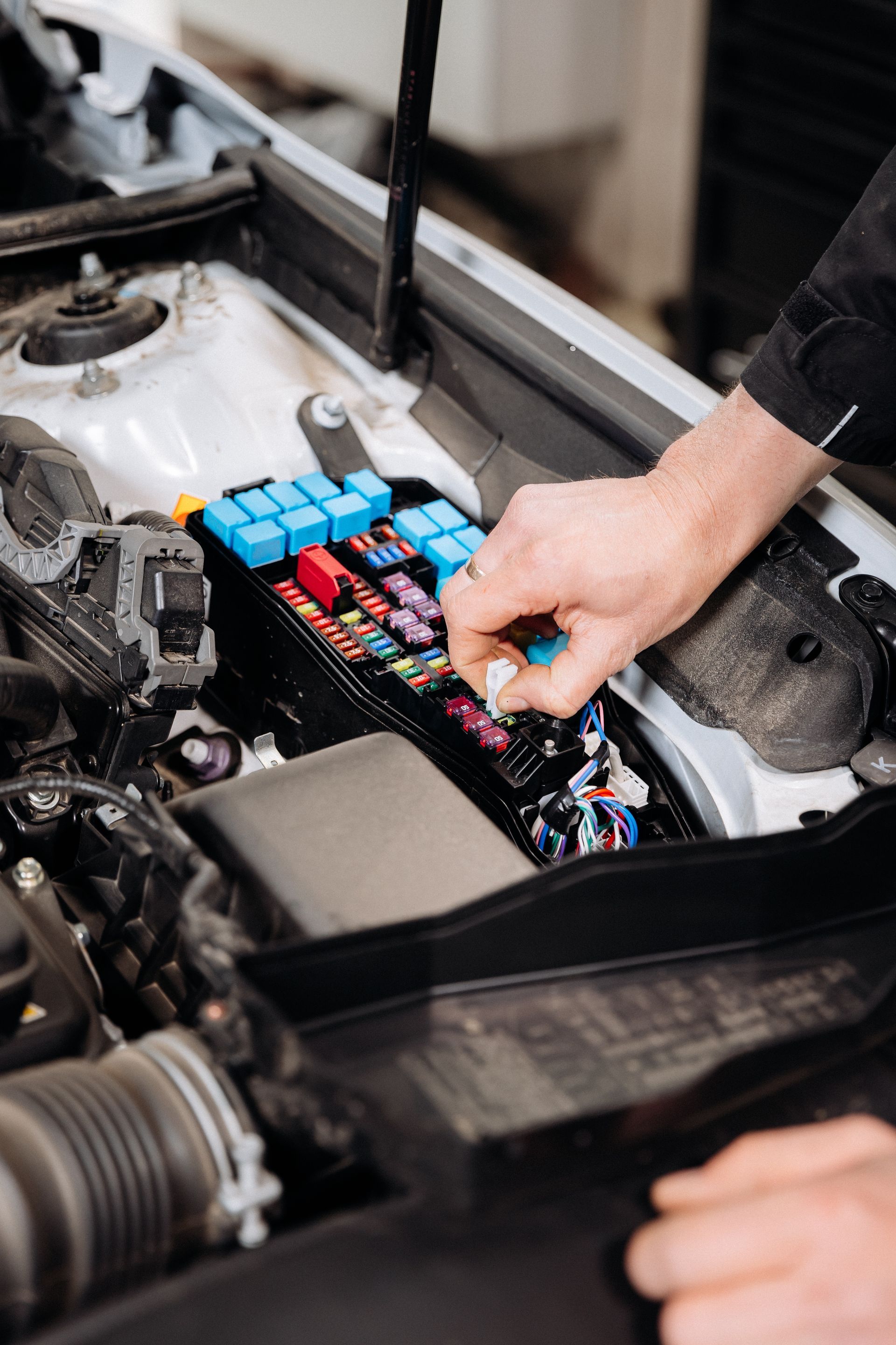 Hand checking colorful fuses in a car’s open engine compartment