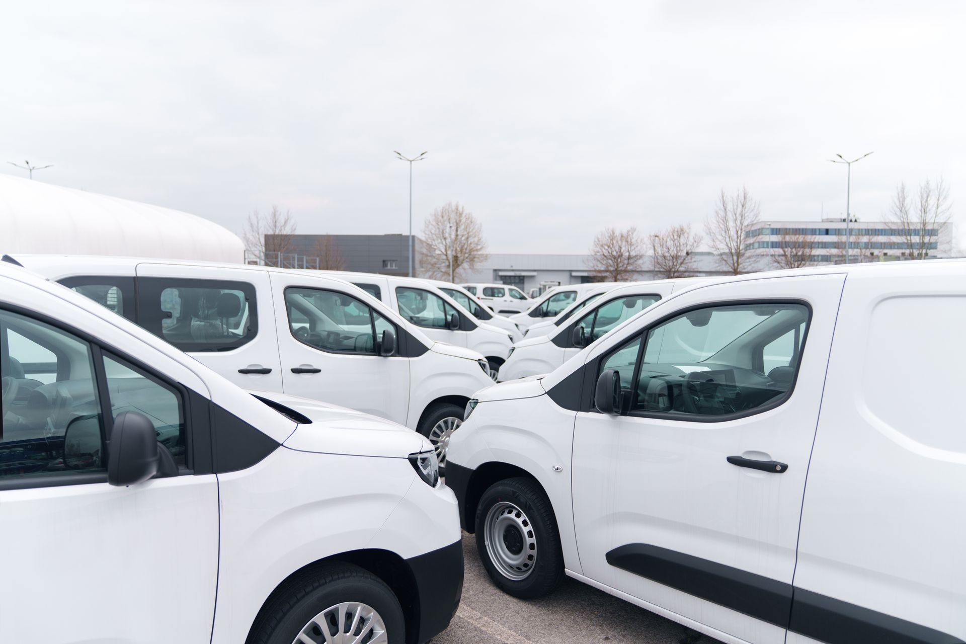 White cargo vans parked closely together in a snowy lot under an overcast sky