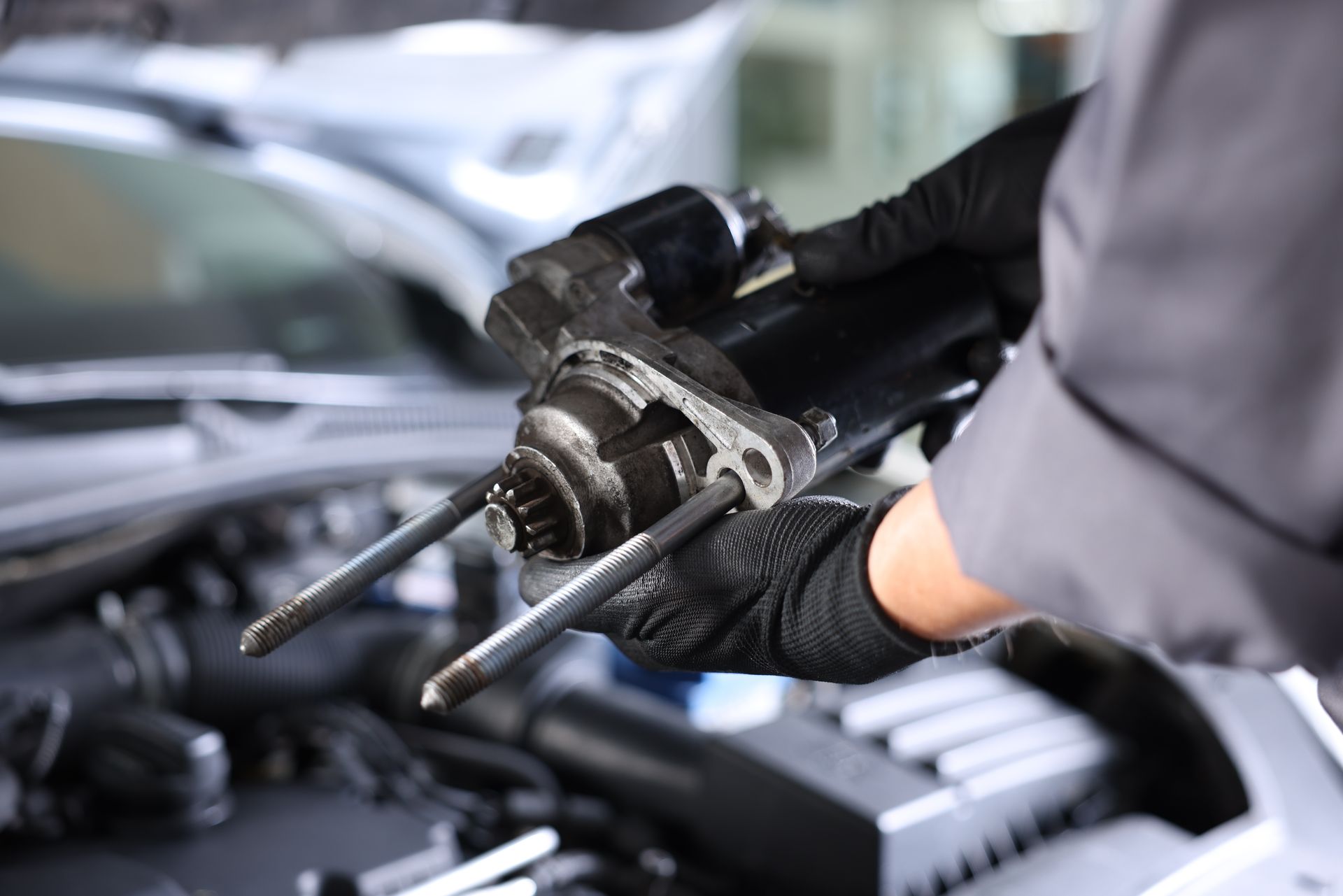 Mechanic’s gloved hands holding a car starter motor over an open engine bay