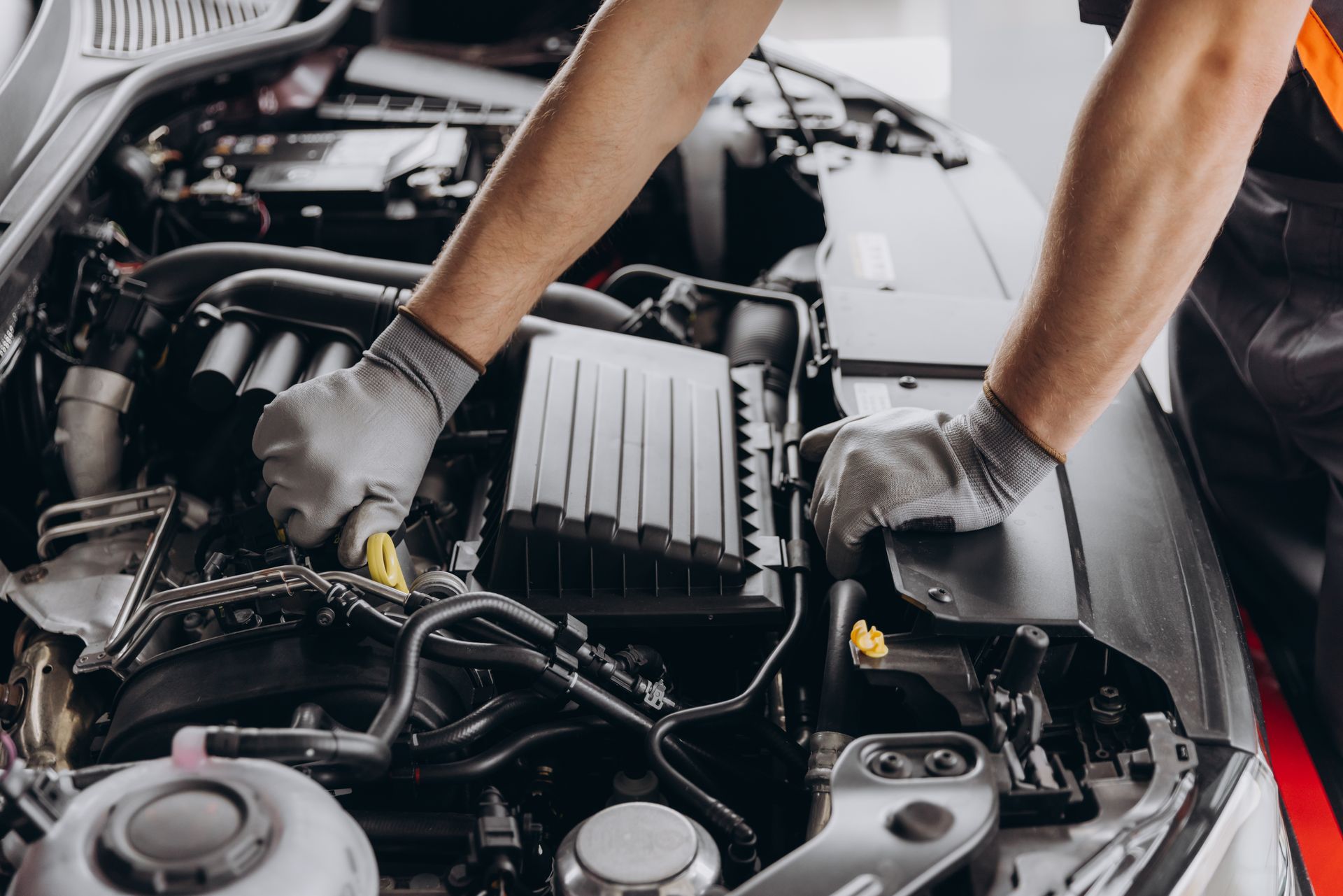 Gloved hands inspecting a car engine under the hood in a garage