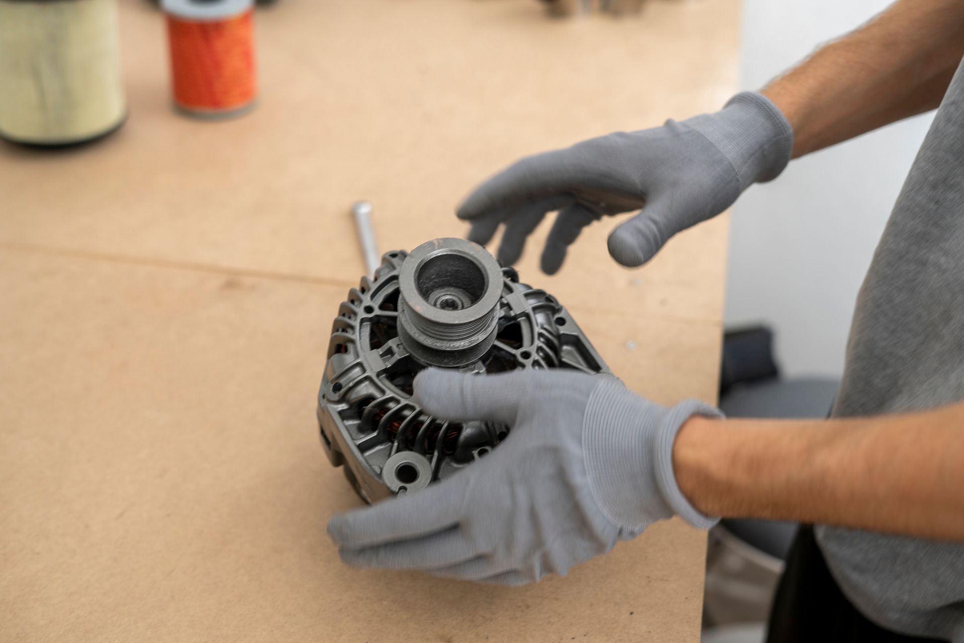 Gloved hands holding an automotive alternator on a workbench