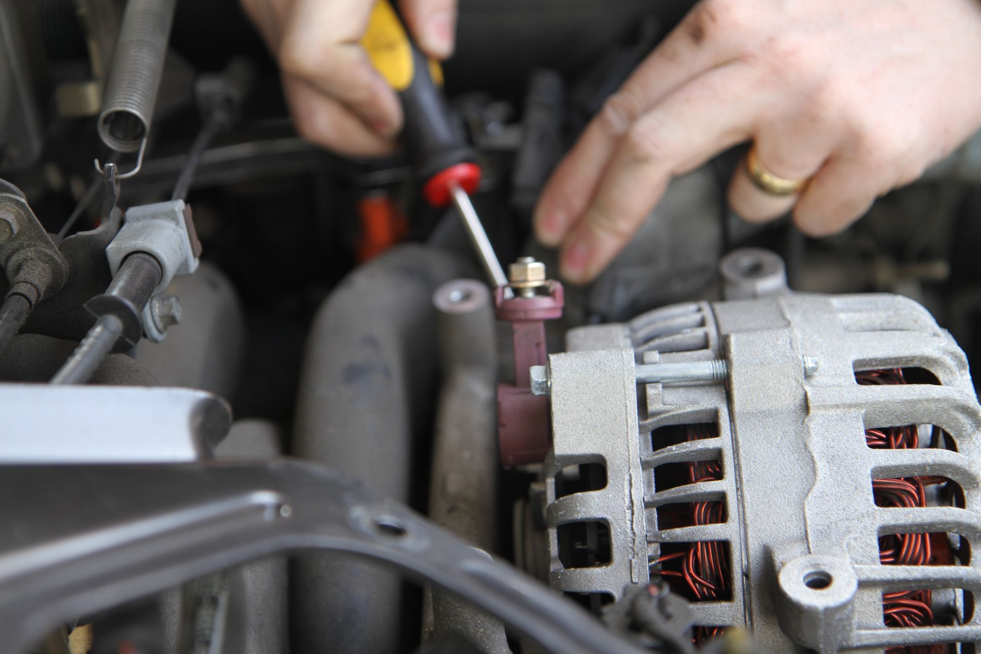 Hands using tools to service a car engine and alternator in a repair shop
