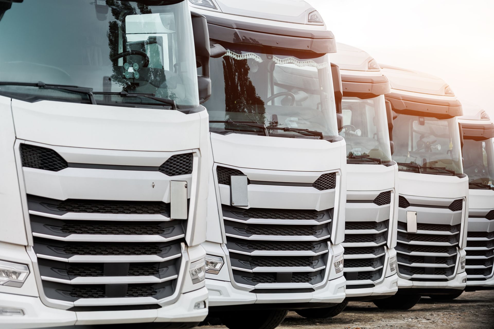 Row of white semi-trucks parked side by side in a lot, front grilles facing forward