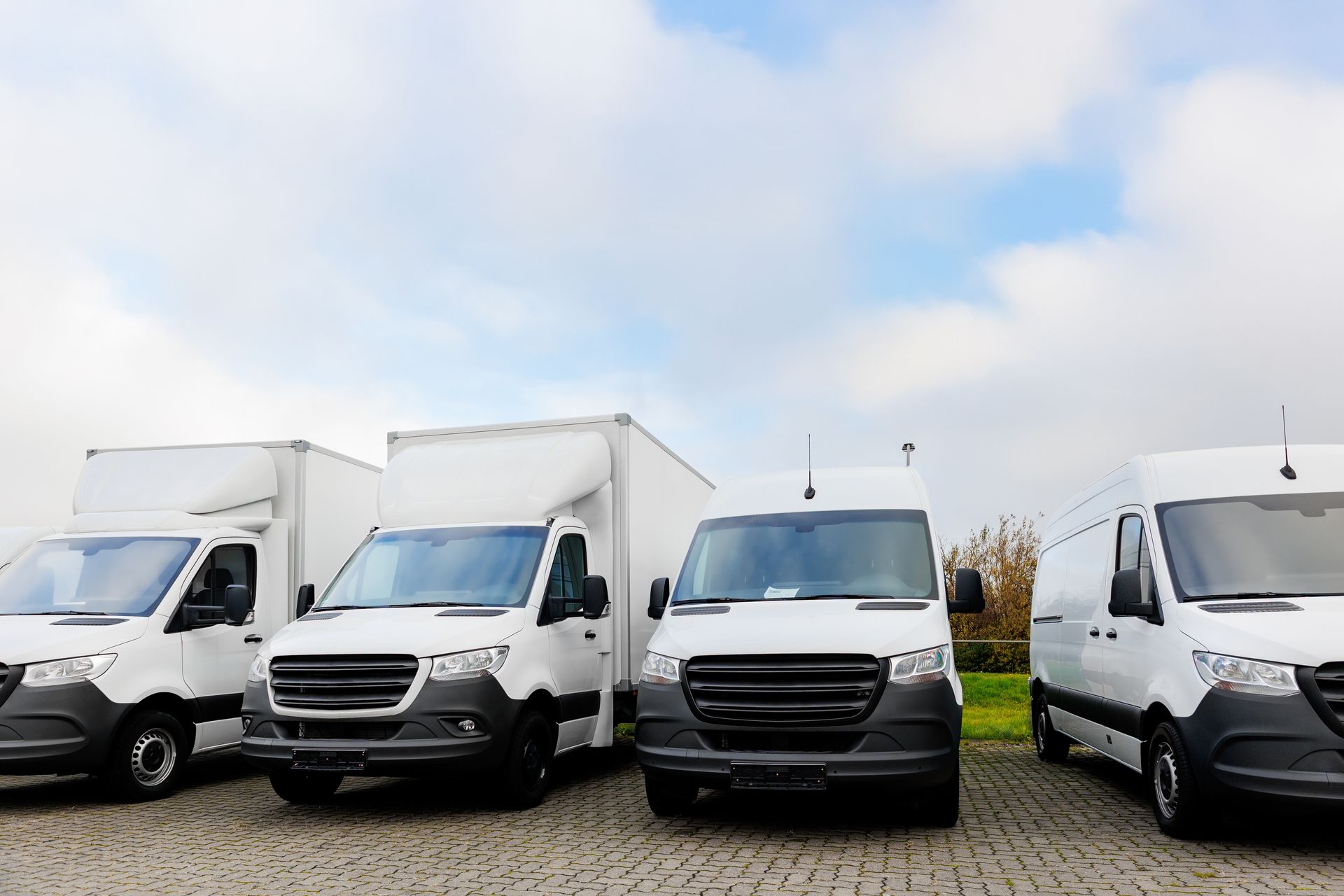 Four white cargo vans parked in a lot under a cloudy sky