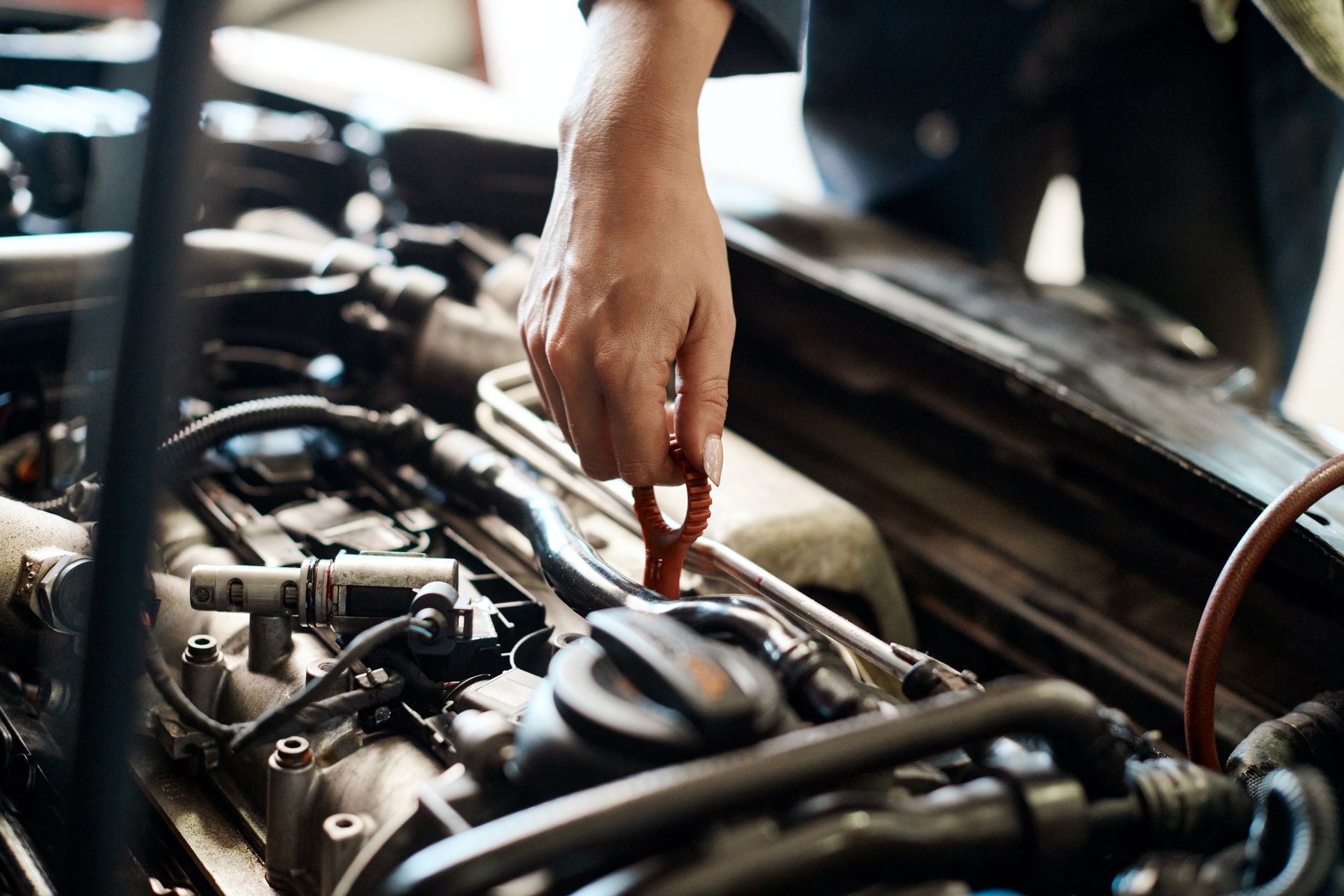 Hand reaching into a car engine bay, inspecting parts with a dipstick or tool