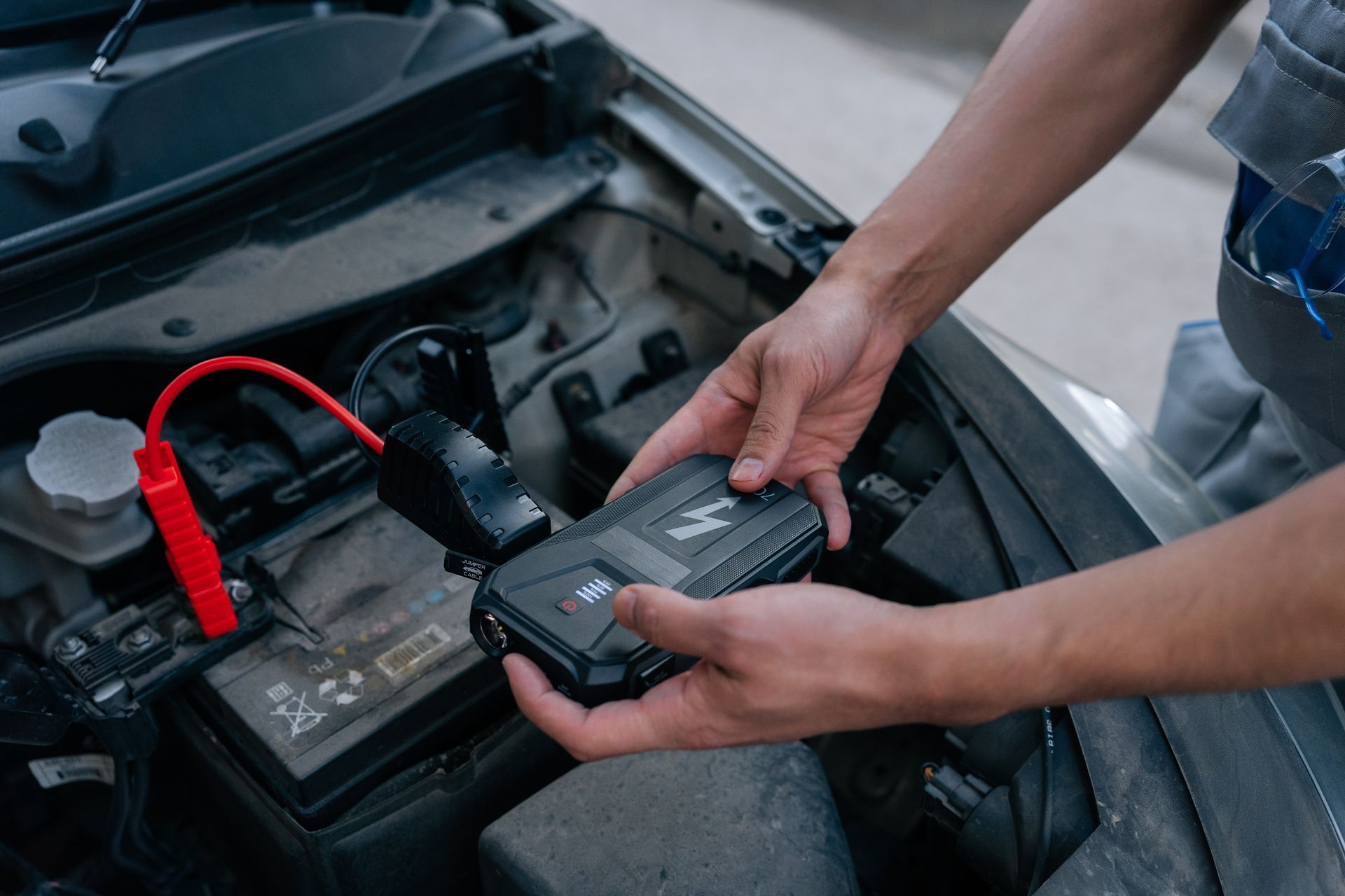 Hands using a jump starter on a car battery in an open engine bay