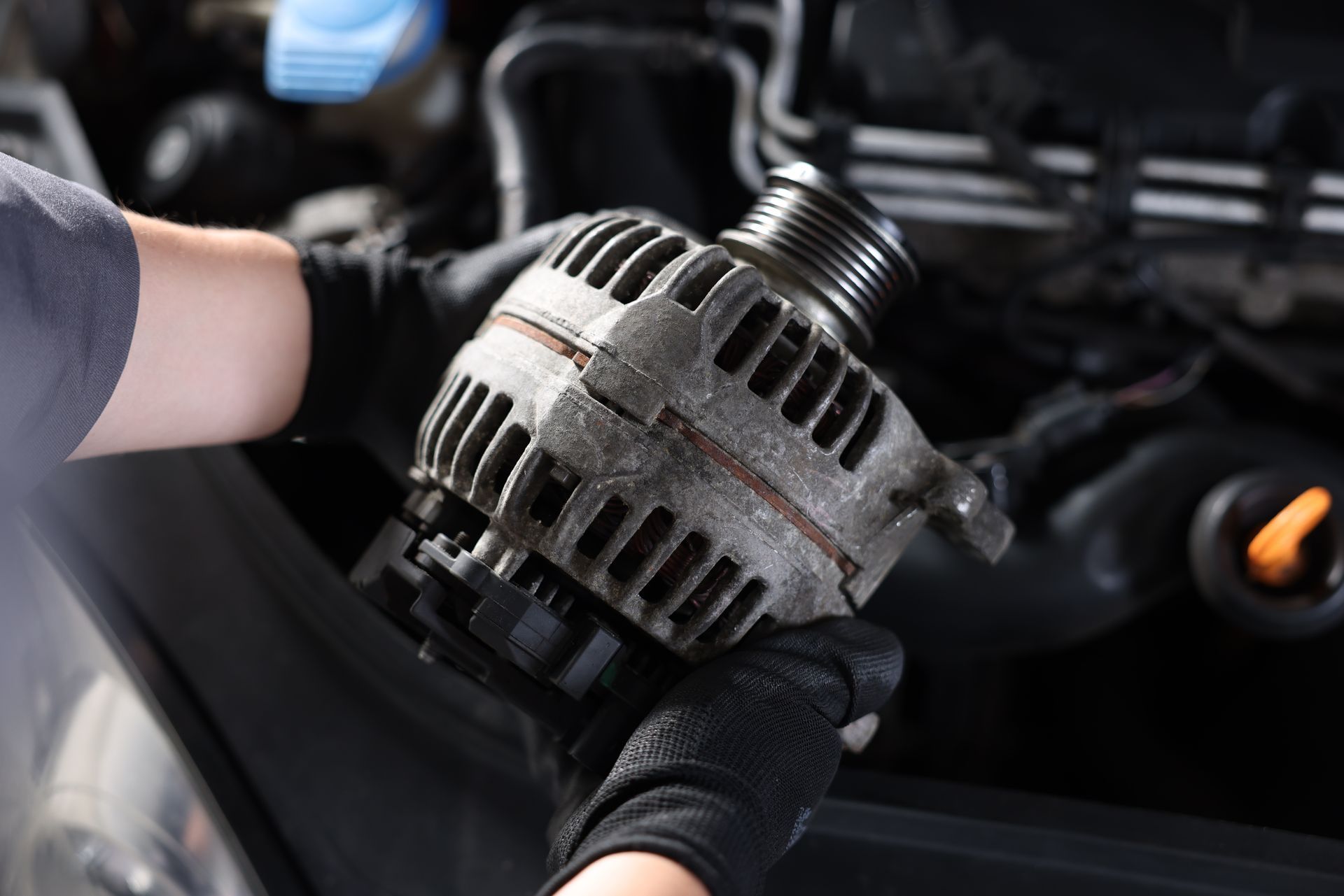 Gloved hands holding a car alternator in an engine bay
