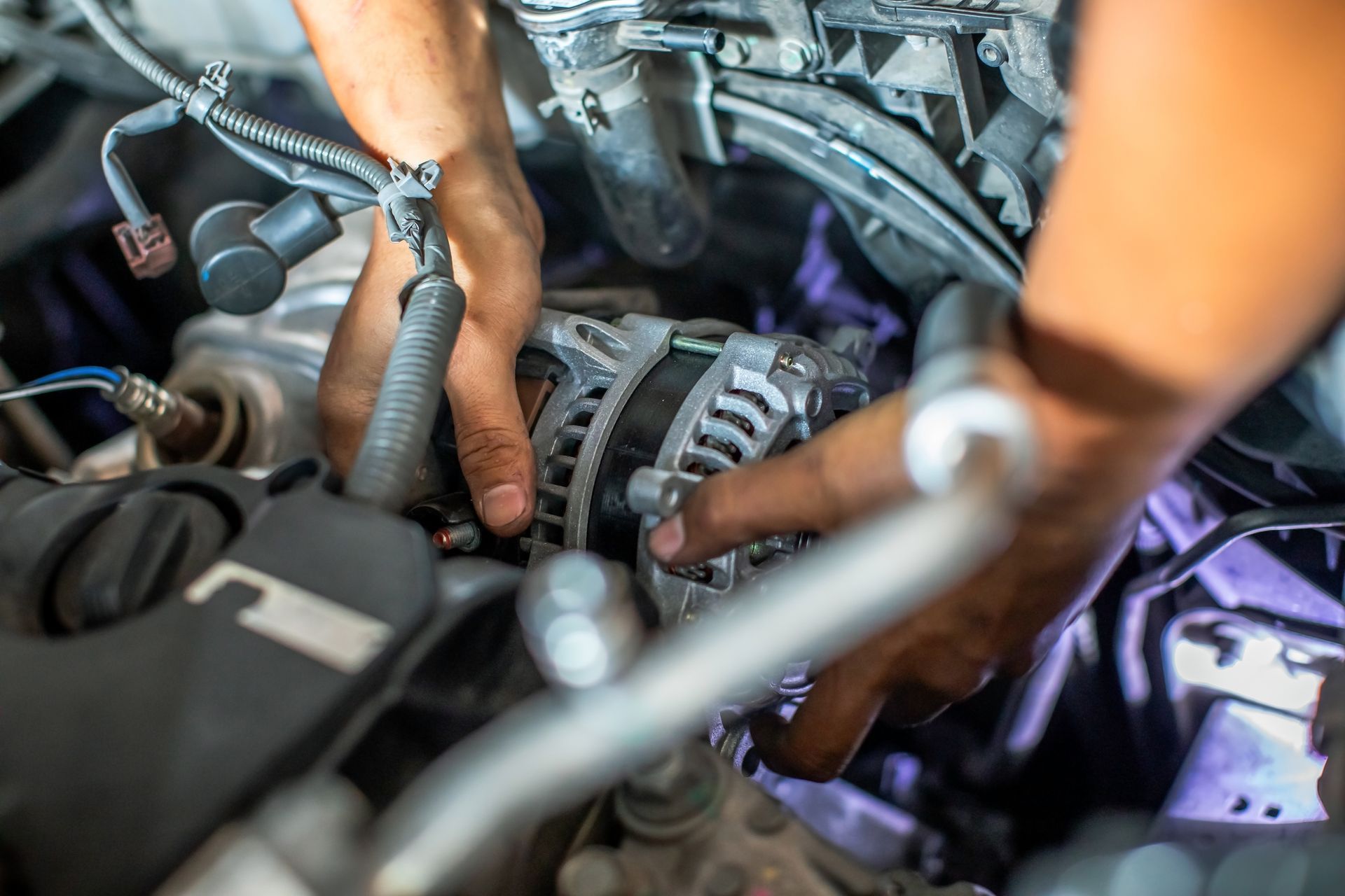 Hands working inside a car engine bay with tools and exposed engine components