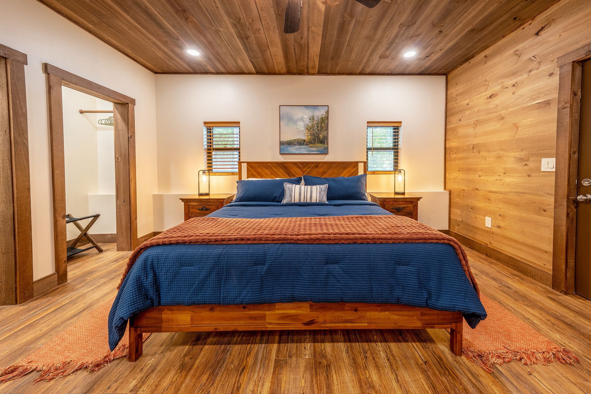 Cozy bedroom with a king bed, blue bedding, wood-paneled walls, and warm ceiling lighting.