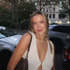 Woman in a white sleeveless dress smiling outdoors beside parked cars at dusk