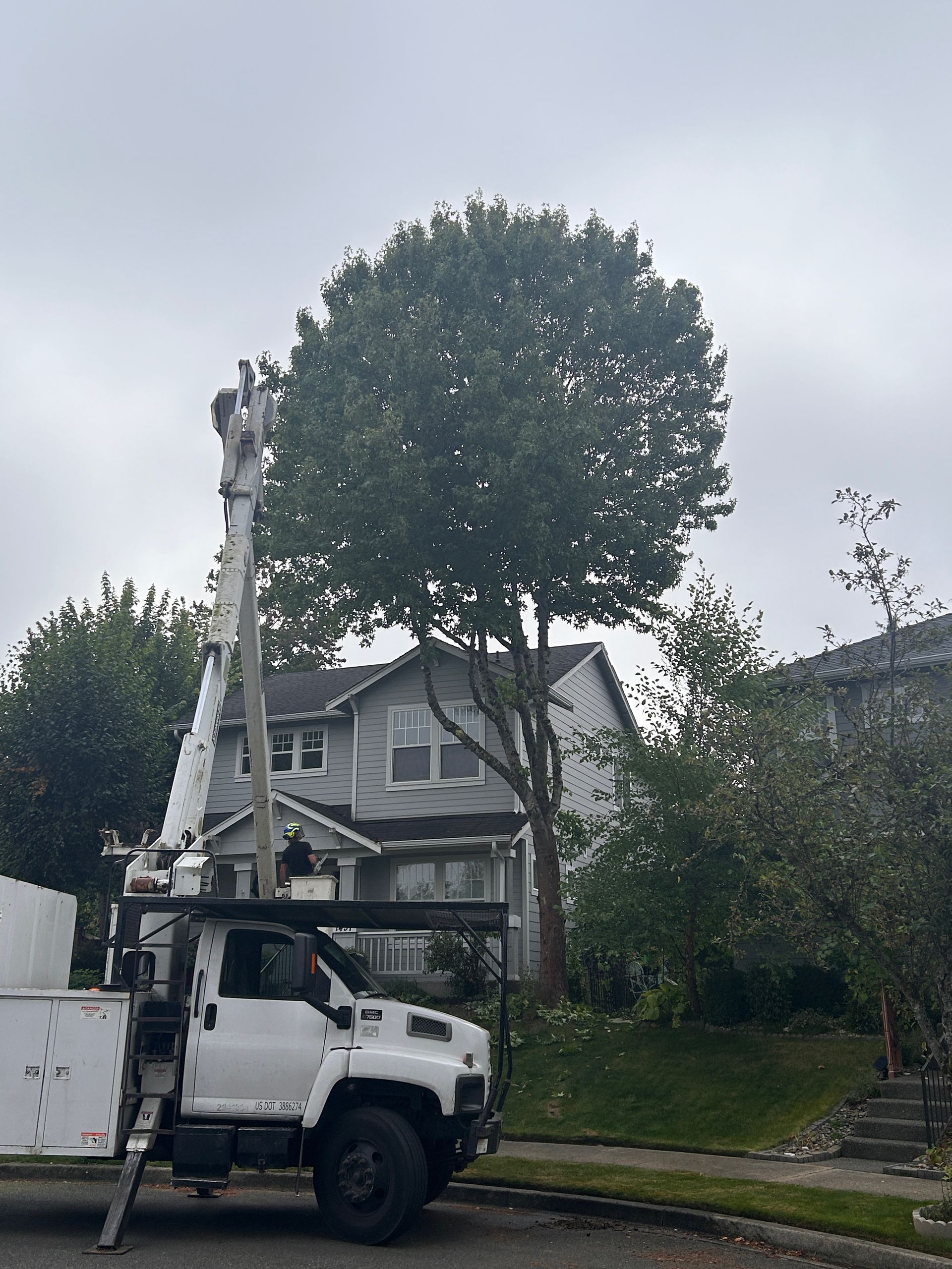 A white truck with a crane on top of it is parked in front of a house.