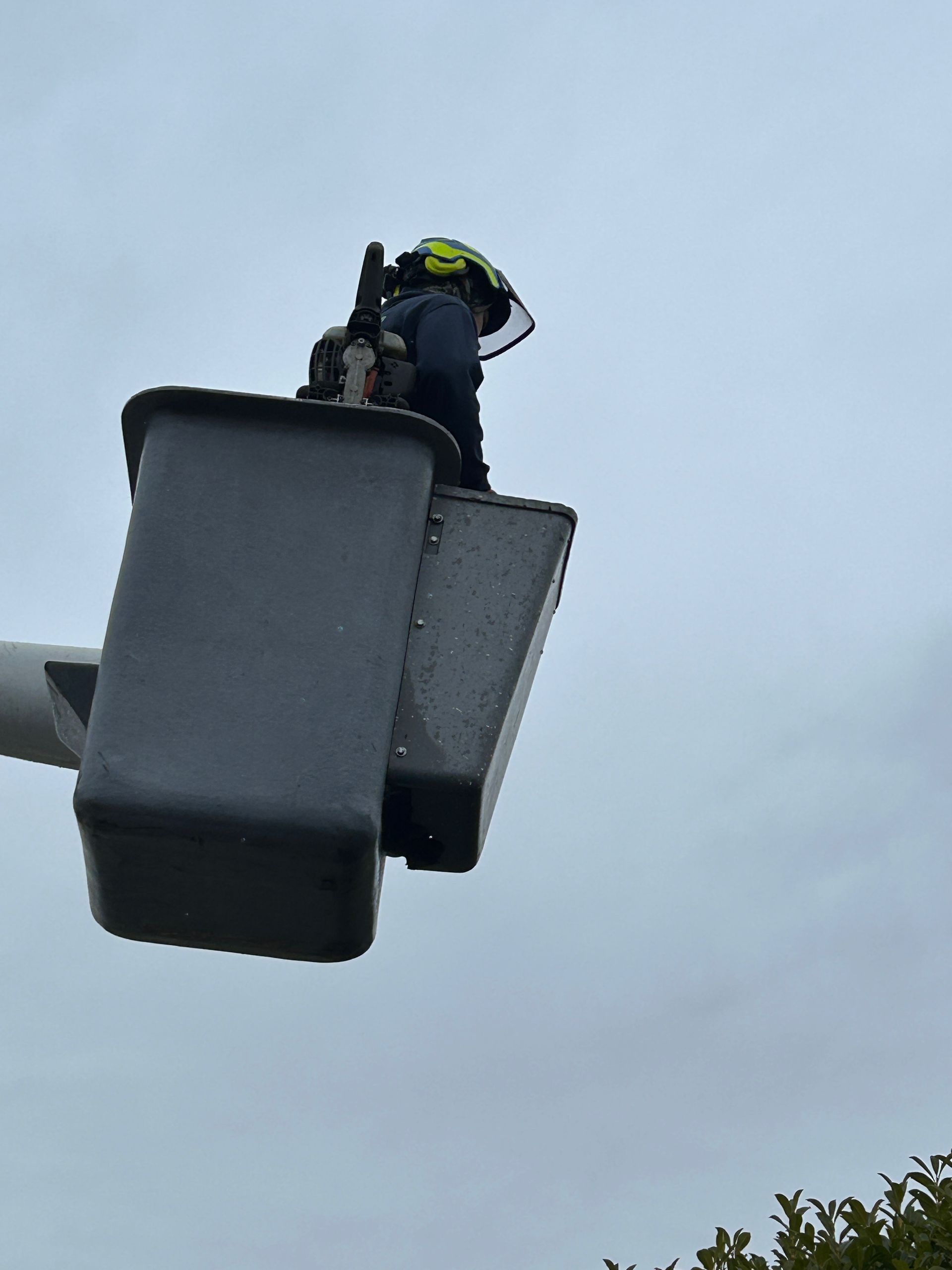 A man in a helmet is standing in a bucket on top of a pole.