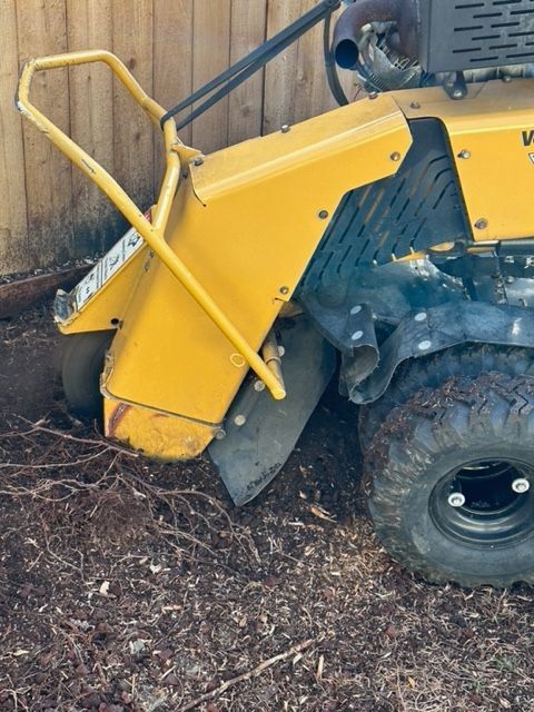 A yellow tractor is sitting in the dirt next to a wooden fence.