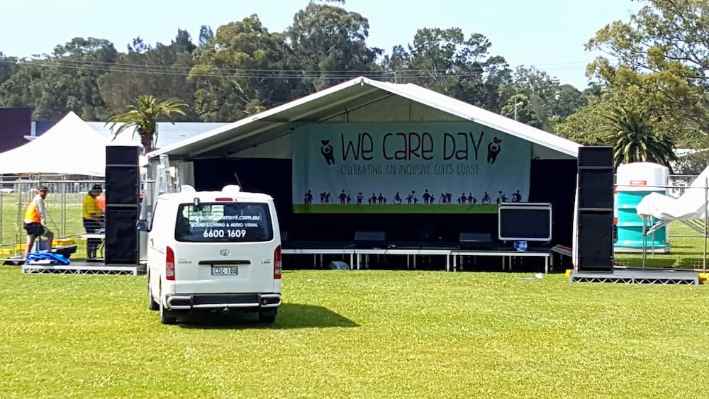 A White Van is Parked in Front of a Stage That Says We Care Day — Inspired Audio Visual in Coffs Harbour, NSW