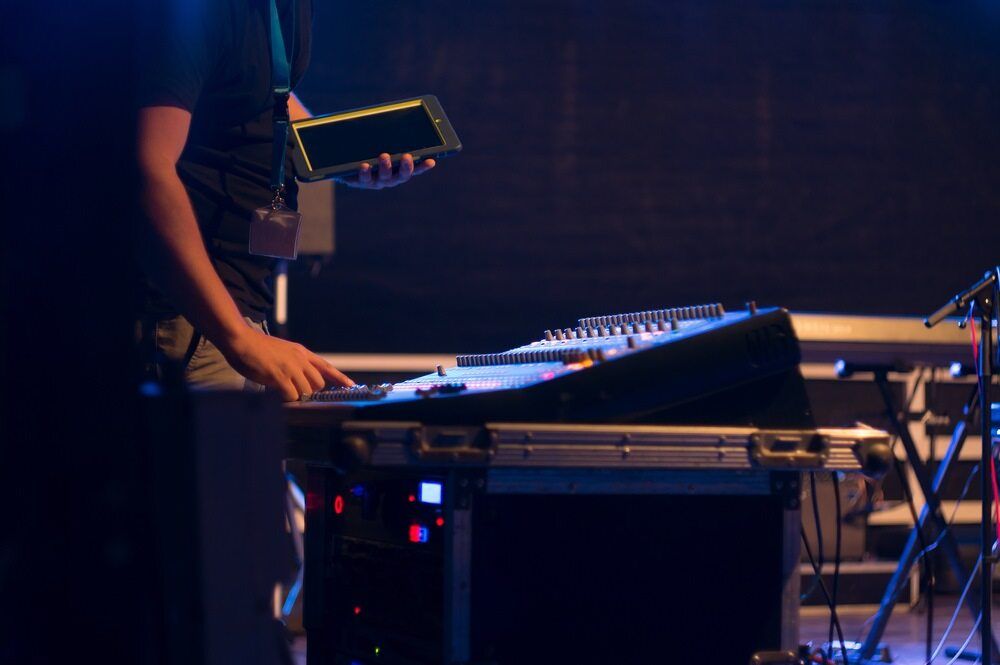 A Man is Standing in Front of a Mixer on a Stage Holding a Tablet — Inspired Audio Visual in Coffs Harbour, NSW
