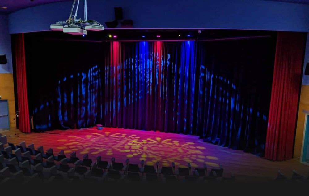 A Large Auditorium With a Red Curtain and a Projector Hanging From the Ceiling — Inspired Audio Visual in Coffs Harbour, NSW