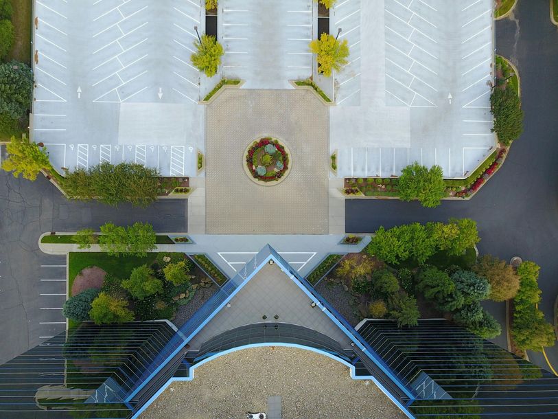 Aerial view of a modern building entrance with white roofs, a central circular planter, and surrounding greenery