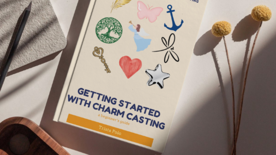 Charm casting guide booklet with colorful symbols on a table beside pom-pom-topped stems