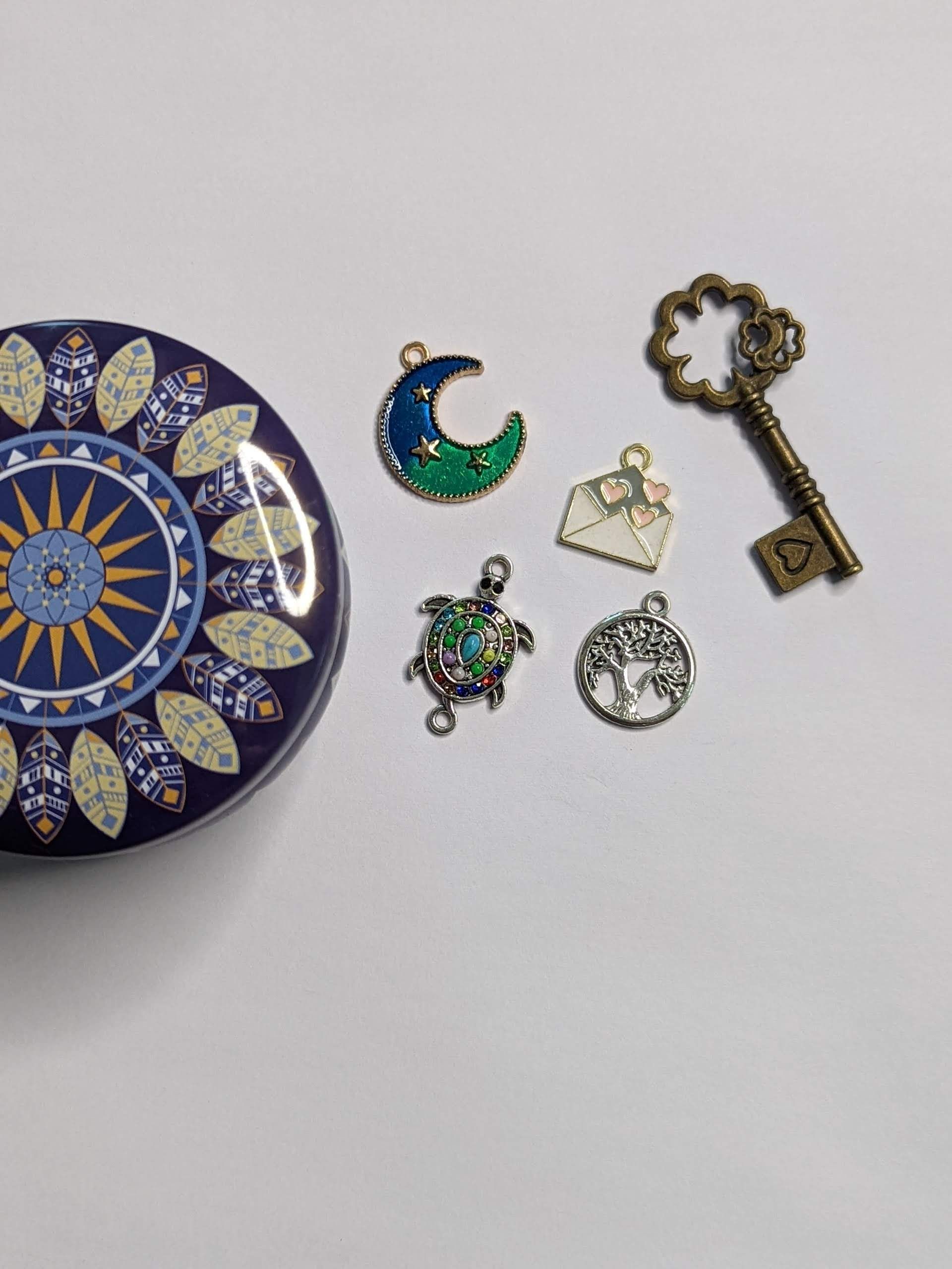 Decorative plate beside small jewelry charms: crescent moon, key, triangle, floral piece, and round pendant