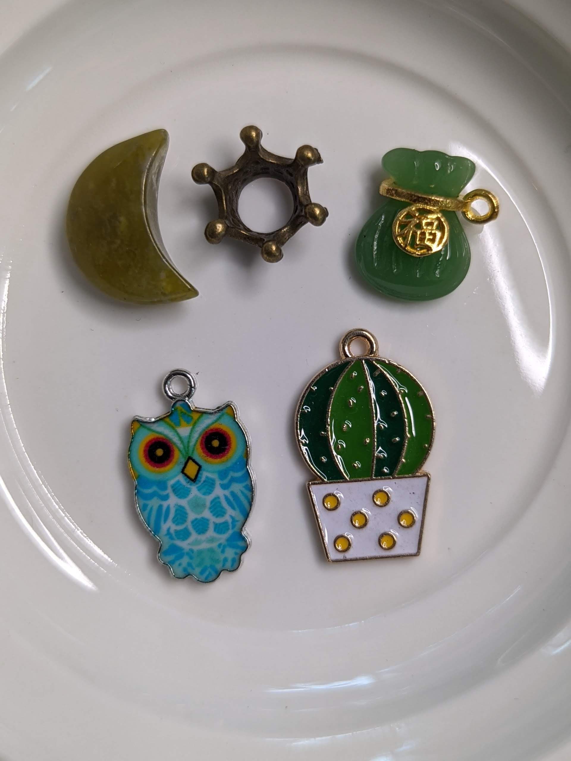 Decorative plate beside small jewelry charms: crescent moon, key, triangle, floral piece, and round pendant